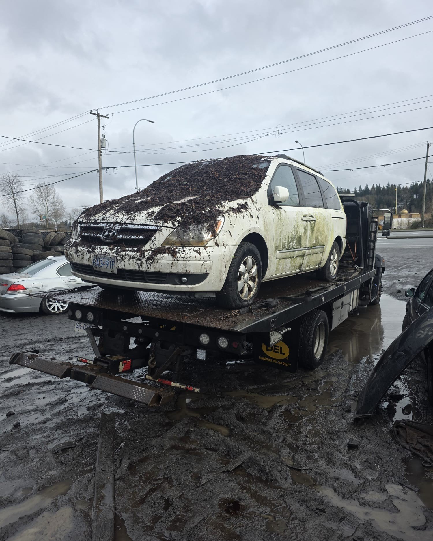 Junk car being winched onto a tow truck on a steep residential driveway near Lions Bay
